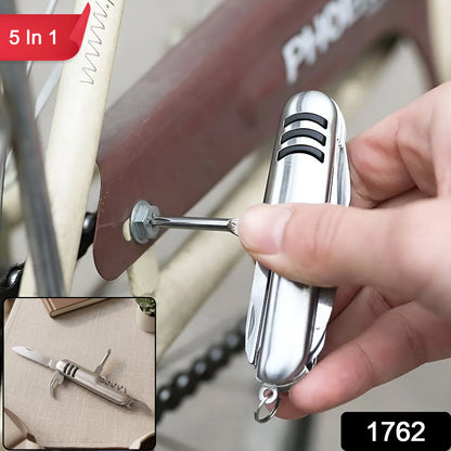 A hand uses the silver multi-tool's corkscrew to remove a cork from a red wine bottle.
