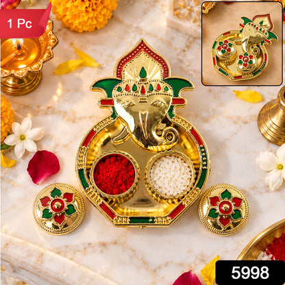 A golden Ganesha-shaped kumkum holder with red powder and white rice on a marble surface, with a small version in the corner.