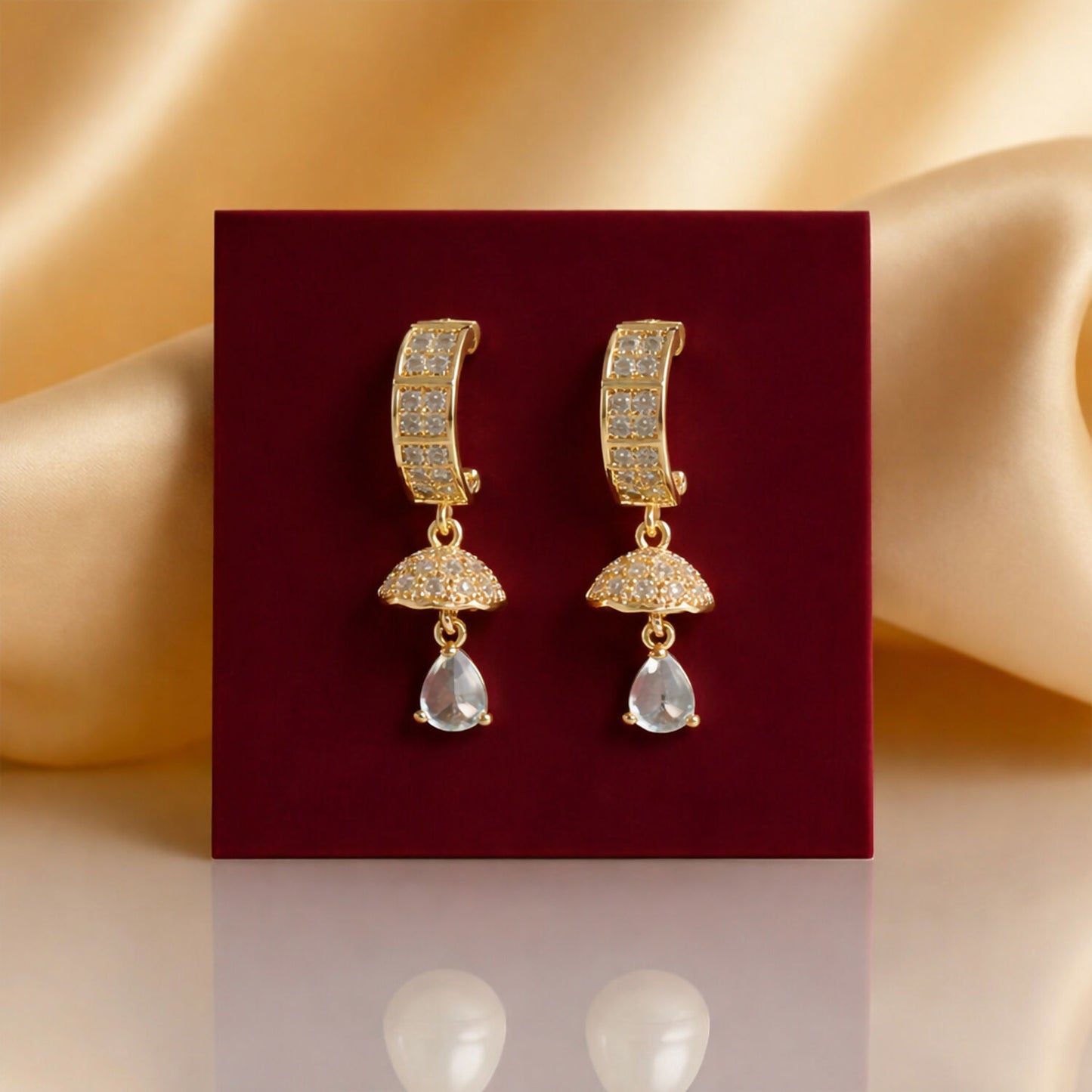 Side angle of elegant gold-tone huggie earrings with teardrop crystal charm