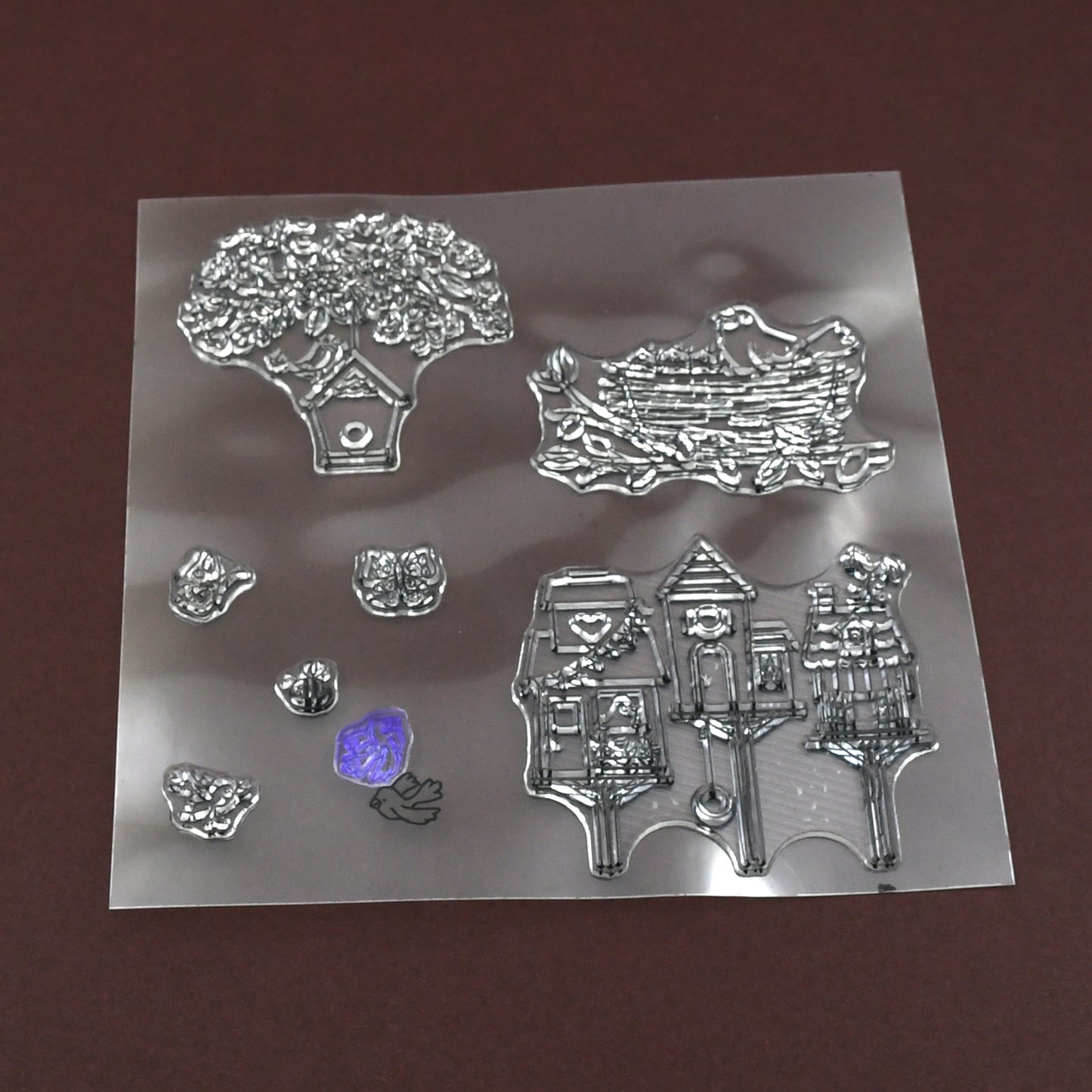 A clear rubber stamp sheet features detailed designs of a tree, bird's nest, and multiple birdhouses.