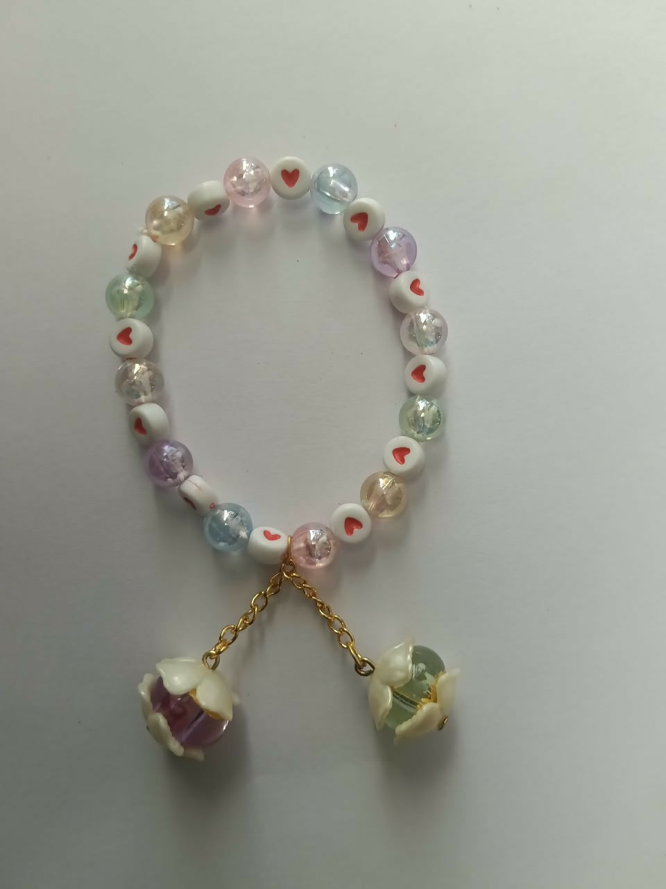 A simple overhead view of the multicolor beaded bracelet with flower charms on a plain light surface.