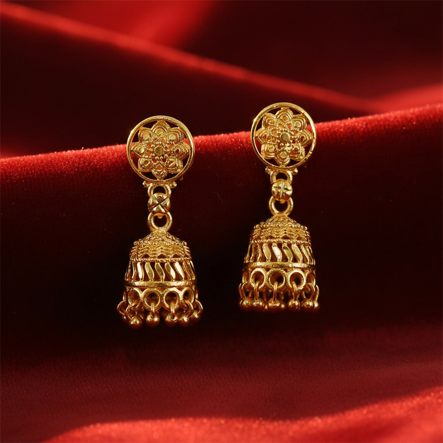 Gold jhumka earrings displayed on a traditional textile background