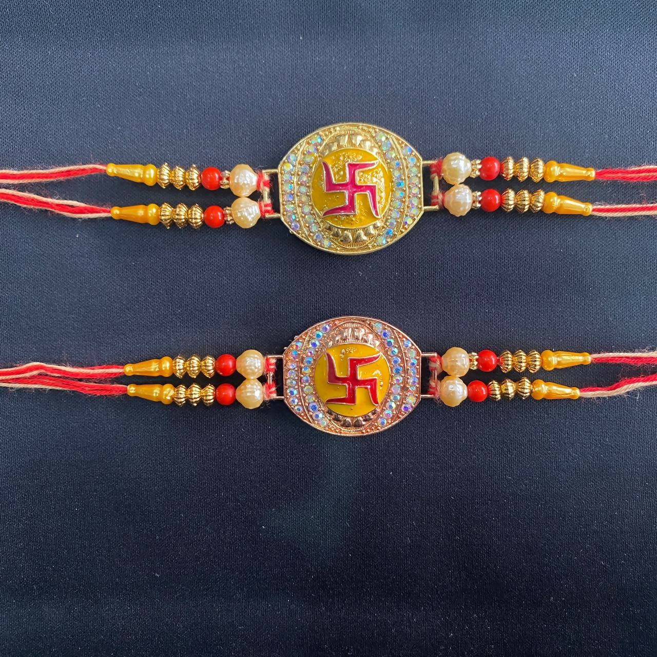 Two gold and rose gold Swastik bracelets with red and yellow threads are presented against a plain black background.