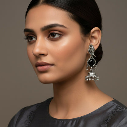 Close-up of oxidized silver jhumka earrings showing detailed owl stud and black stone centerpiece