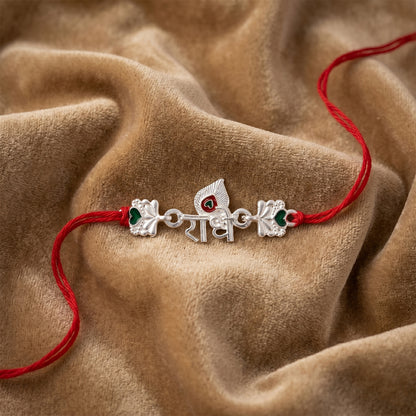 Silver Radhe Morpich Text Rakhi with Green Stones and Red Thread