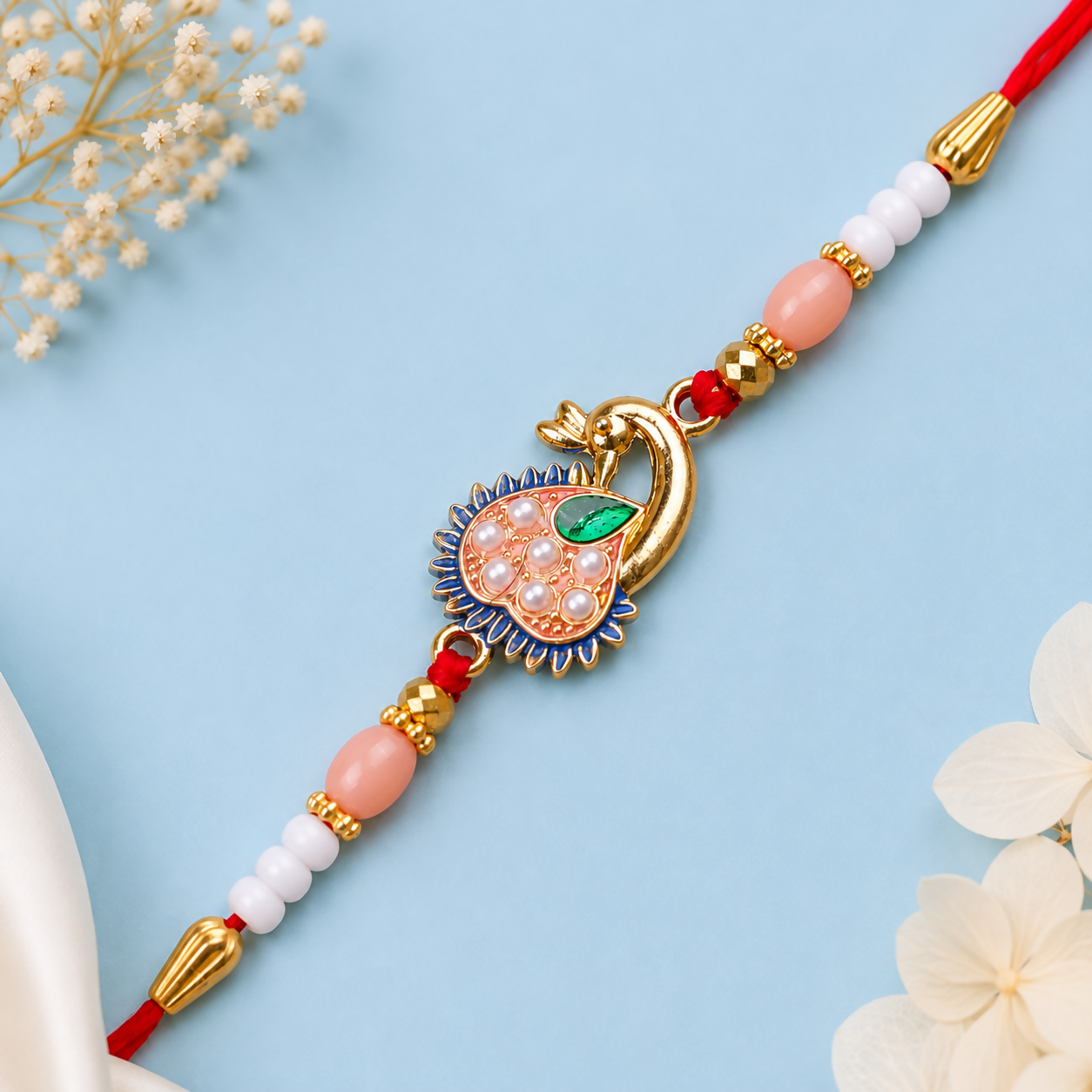 A red thread with a gold peacock charm, pink and white beads, and gold accents, on a light blue background with white