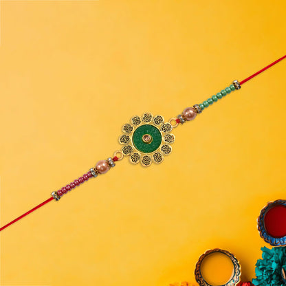 Hand holding floral rakhi with green centerpiece and multicolor beads