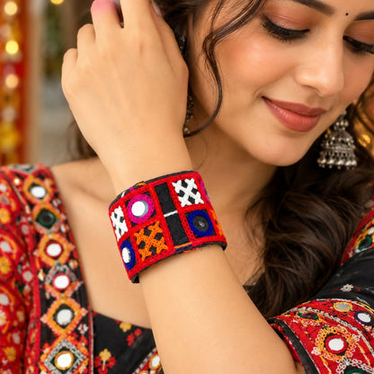 A woman wears a wide black fabric cuff bracelet with red, pink, blue, orange embroidery and small mirrors.