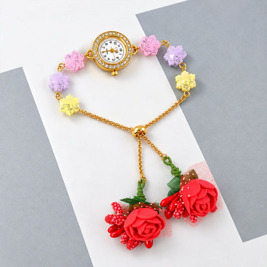 Gold-toned watch with a rhinestone bezel, multicolor flower links, and two dangling red fabric rose charms.