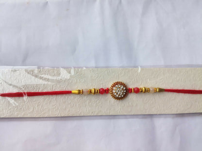 A red and gold bracelet with a central crystal medallion is presented on a textured white card against a plain background.