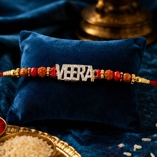 Close-up of Veera name golden designer rakhi with red stones and pearl accents.