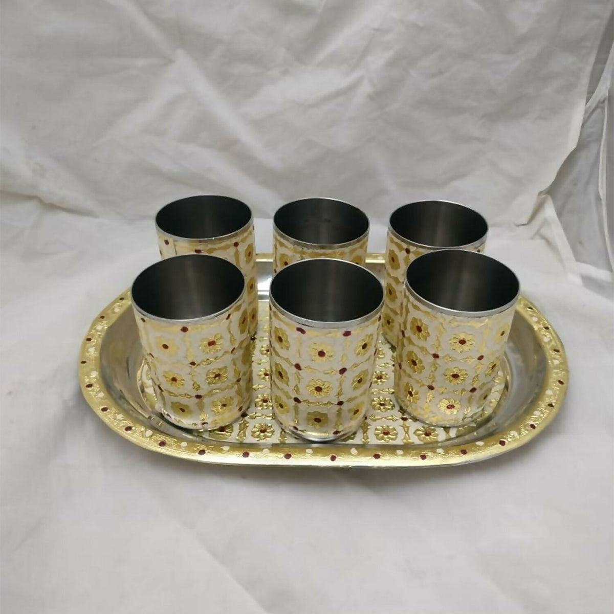Six stainless steel glasses with a yellow and red floral pattern on a matching oval tray, on a white cloth.