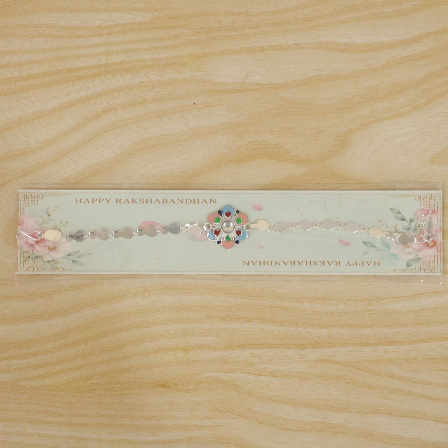 A silver chain rakhi with a colorful enamel flower charm on a