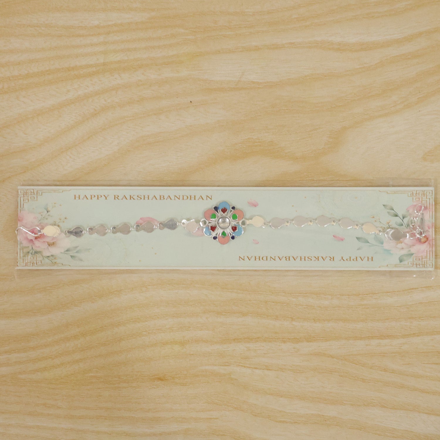 A silver chain rakhi with a colorful enamel flower charm on a