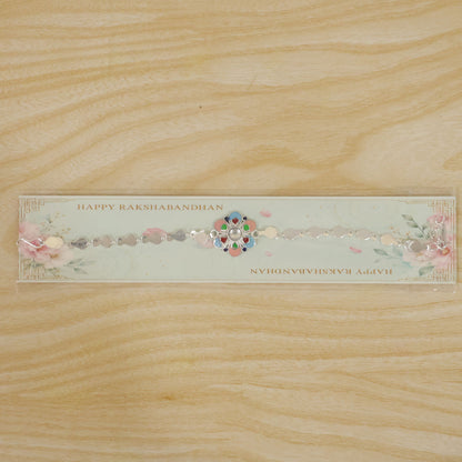 A silver chain rakhi with a colorful enamel flower charm on a