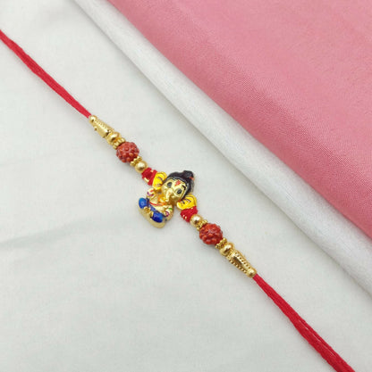 A red thread with a metallic Ganesha charm and red carved beads is displayed on a white and pink fabric background.