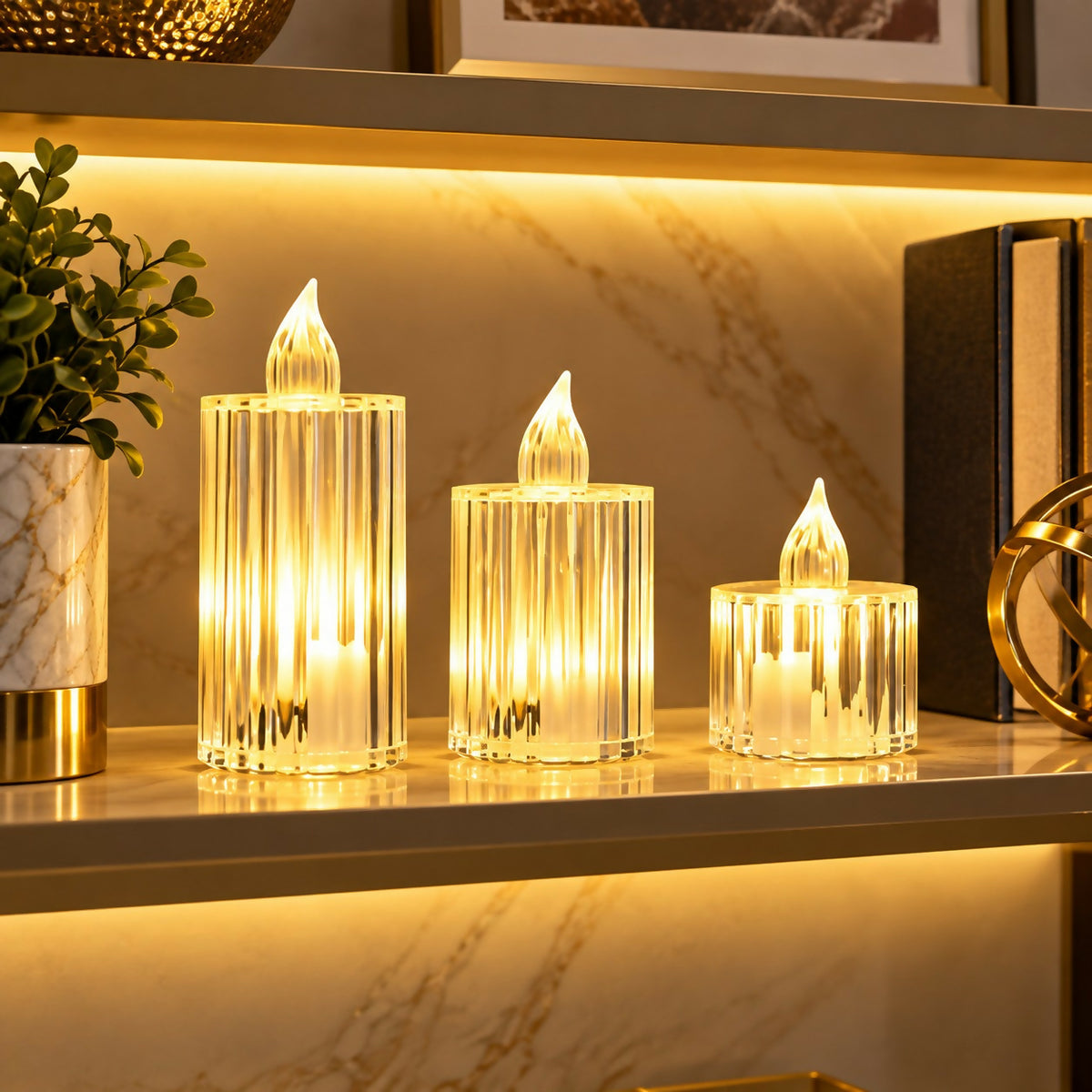 Three illuminated crystal-look LED candles of varying heights on a gold shelf with a plant and books.