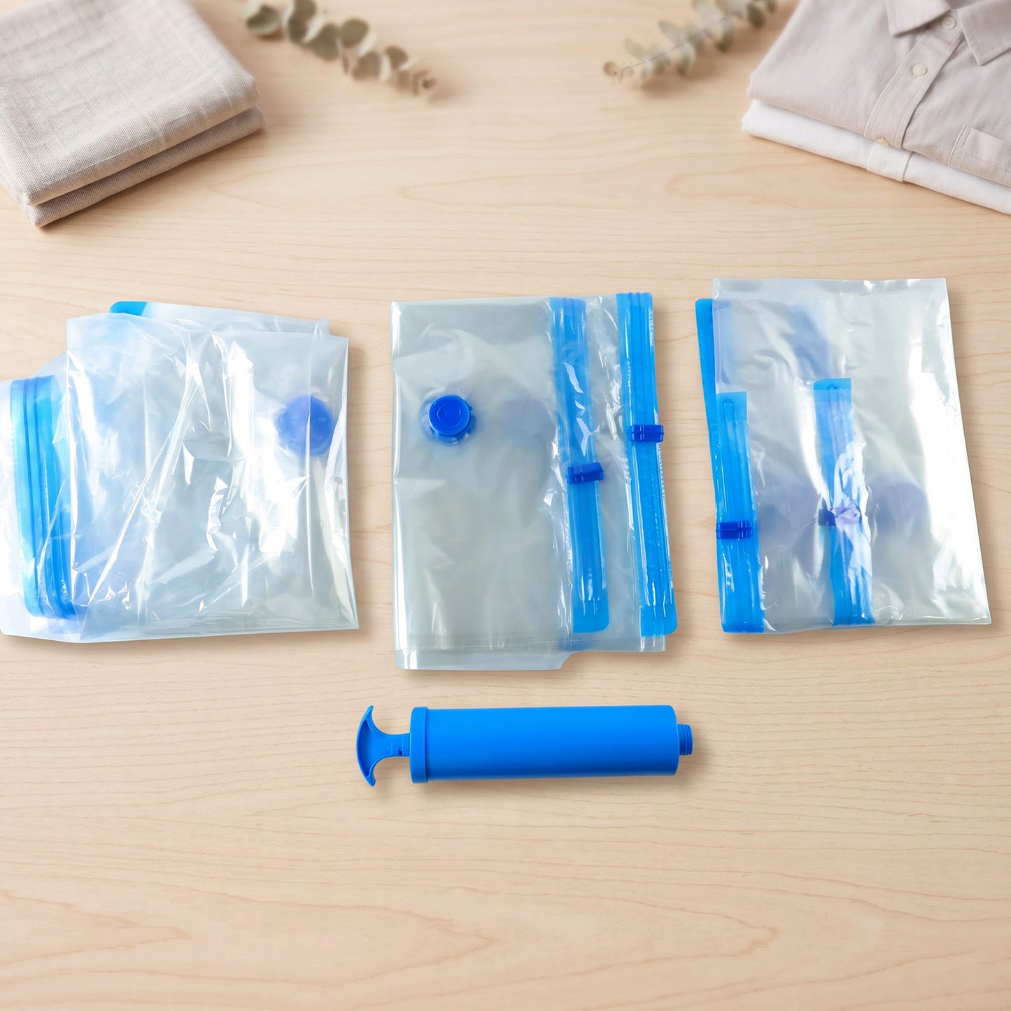 Three clear vacuum storage bags with blue accents and a blue hand pump are laid out on a light wooden surface.