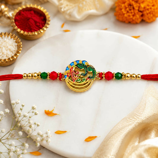 A gold, red, green, and blue Meenakari peacock and Ganesha circular dial is centered on a red thread with gold and crystal