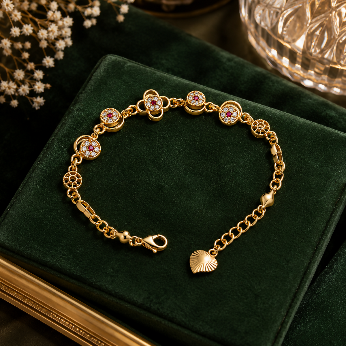 A gold-plated bracelet with floral charms featuring red and clear gemstones rests on a dark green velvet surface.