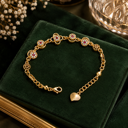 A gold-plated bracelet with floral charms featuring red and clear gemstones rests on a dark green velvet surface.