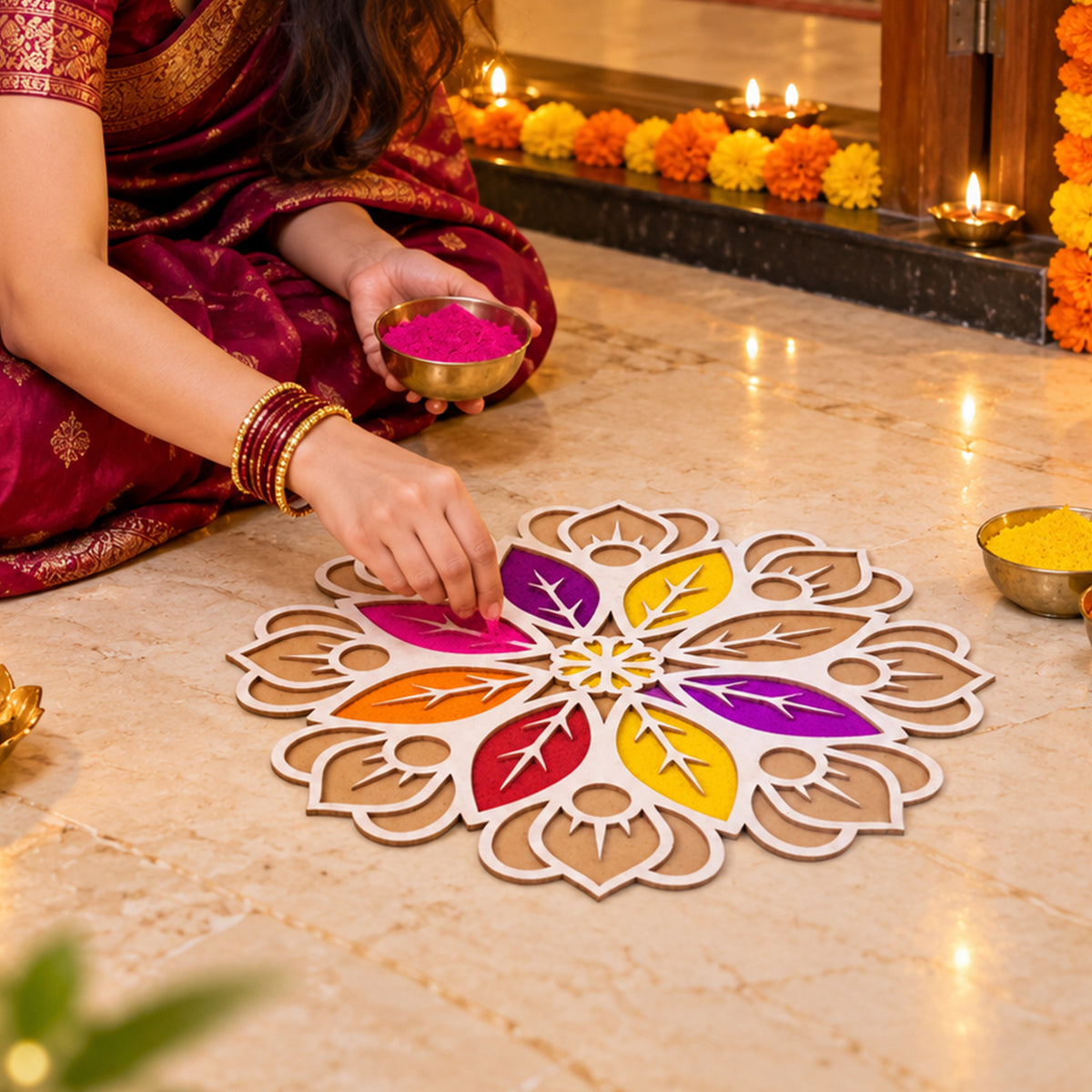 A woman in a maroon sari sits on the floor, filling a white and brown rangoli stencil with vibrant purple powder from a