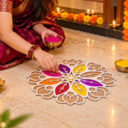 A woman in a maroon sari sits on the floor, filling a white and brown rangoli stencil with vibrant purple powder from a