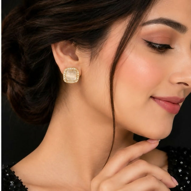 A woman models a single square stud earring with a clear stone and a sparkling border on her earlobe.