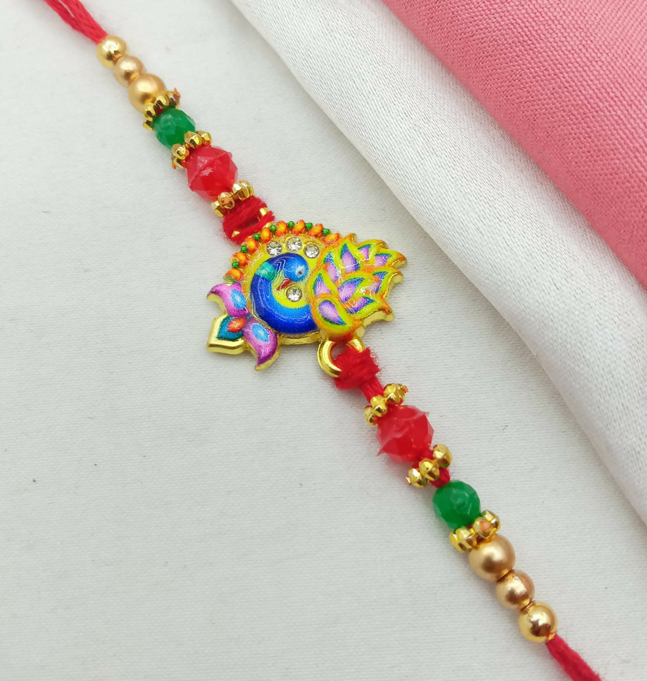 A close-up of a golden-plated peacock enamel design with crystal stones and beaded thread on a white and pink fabric