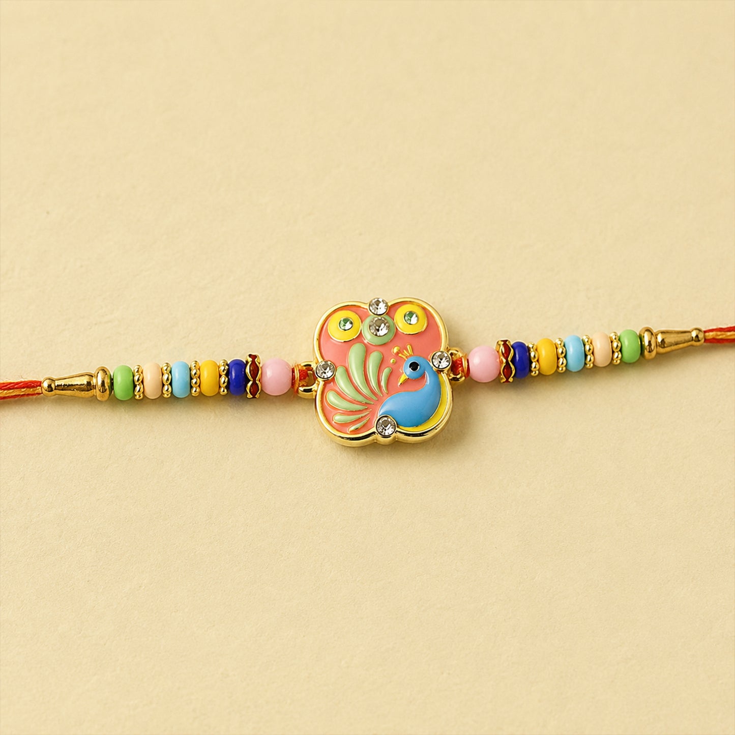 A vibrant peacock design with a pink background and blue bird, adorned with clear beads, sits on a red thread with colorful