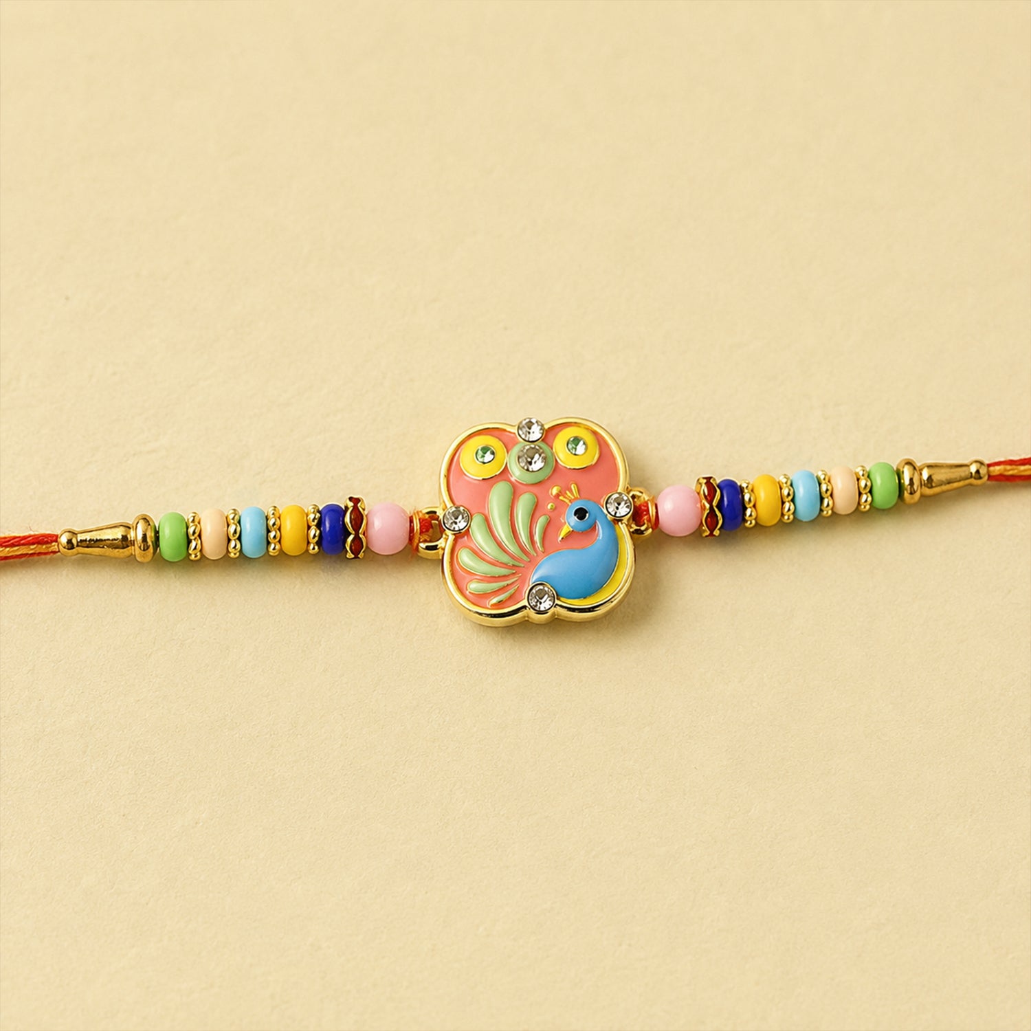 A vibrant peacock design with a pink background and blue bird, adorned with clear beads, sits on a red thread with colorful