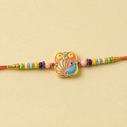 A vibrant peacock design with a pink background and blue bird, adorned with clear beads, sits on a red thread with colorful