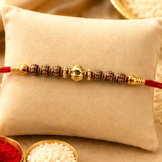 A red thread bracelet with gold and dark brown patterned beads rests on a light tan cushion, with small bowls of red powder