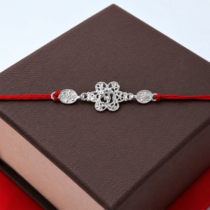 Close-up of silver floral Om rakhi design with red thread