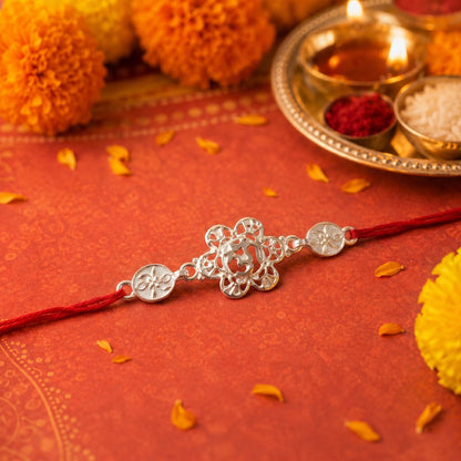 Silver floral Om rakhi displayed on wooden surface