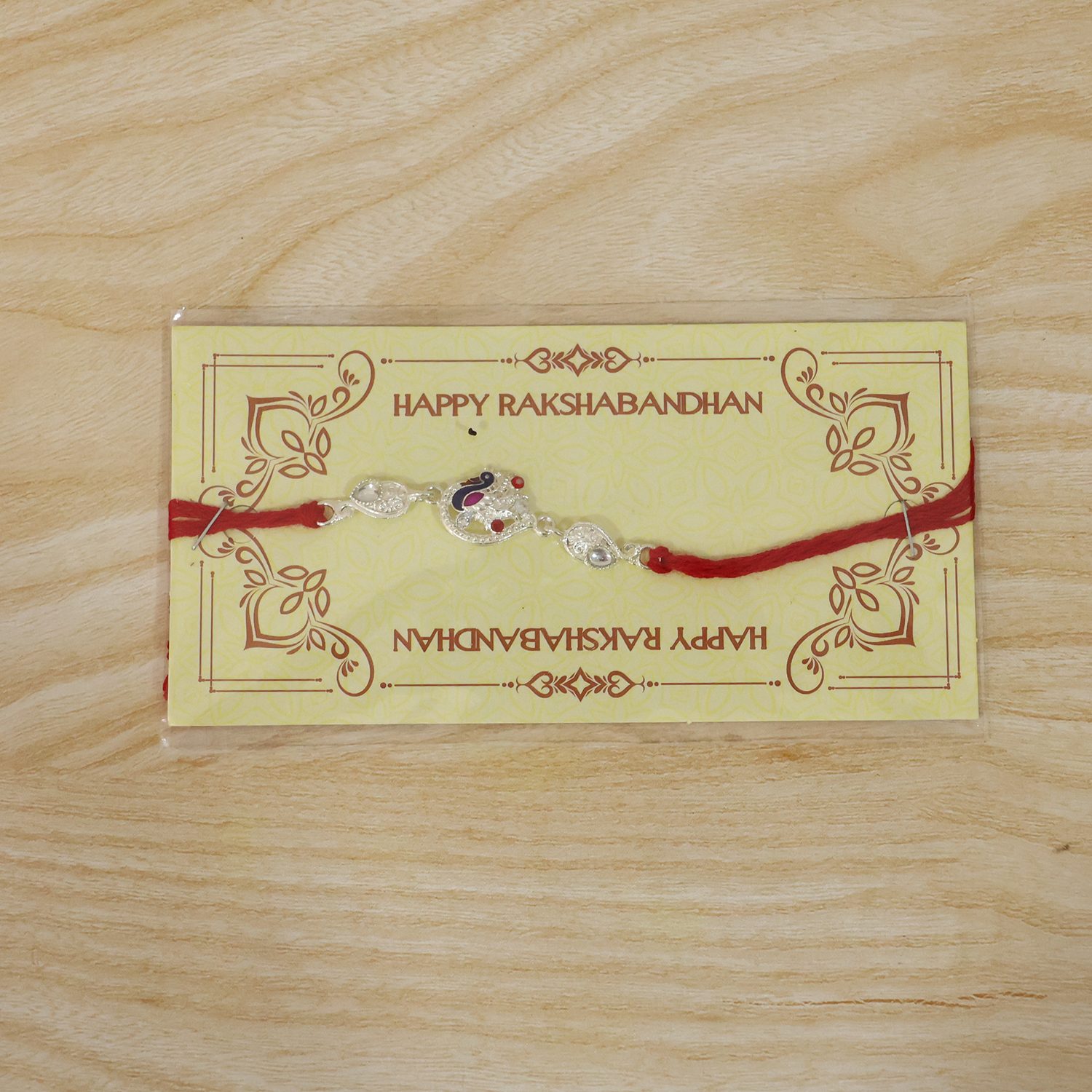 Silver peacock charm rakhi with vibrant red thread
