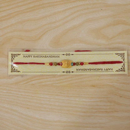Hand holding Lord Ganesha gold-plated rakhi with red beads