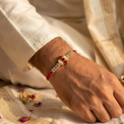 Gold rakhi with pink stone & AD studs tied on a brother's wrist