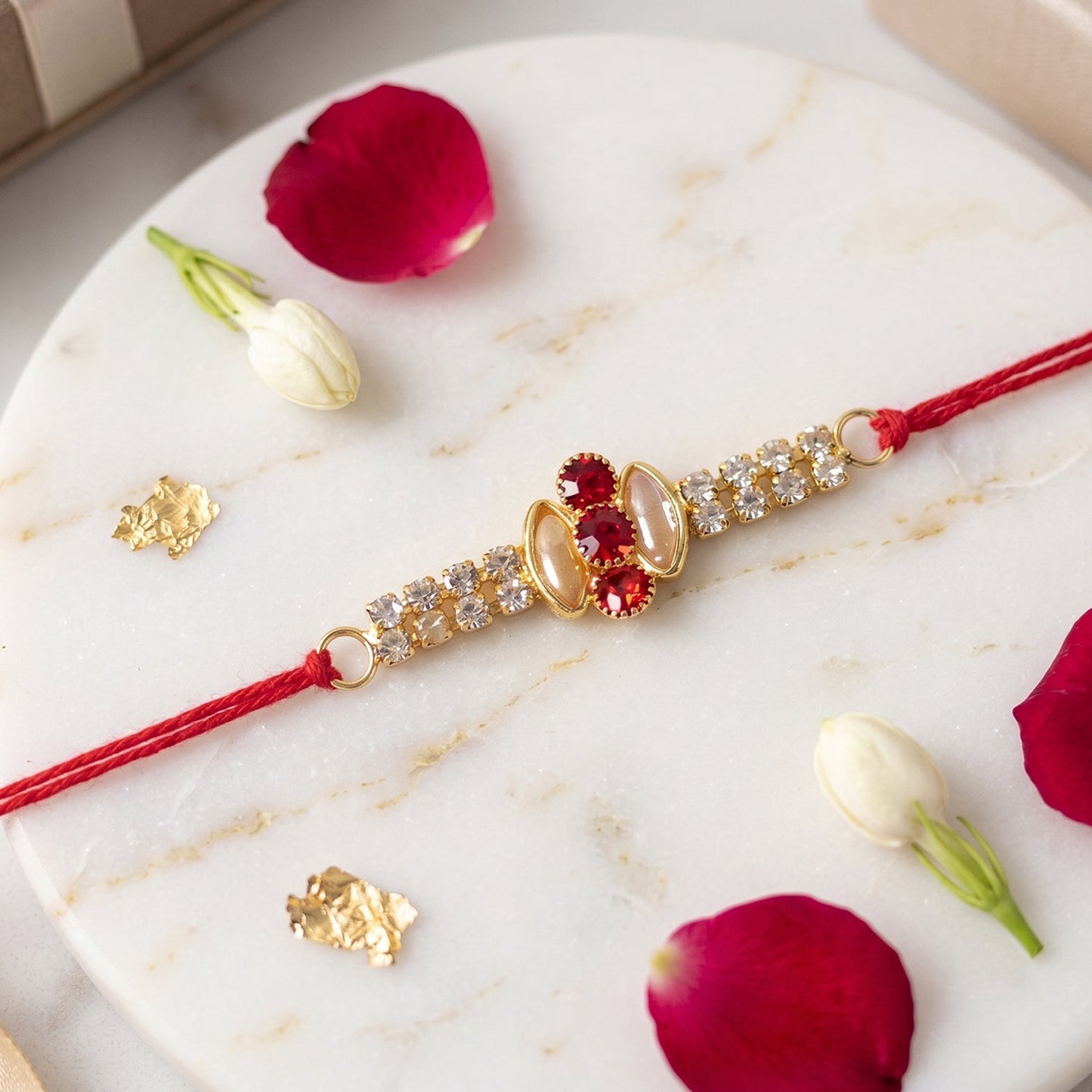 Gold rakhi with pink stone & AD studs displayed on a festive surface