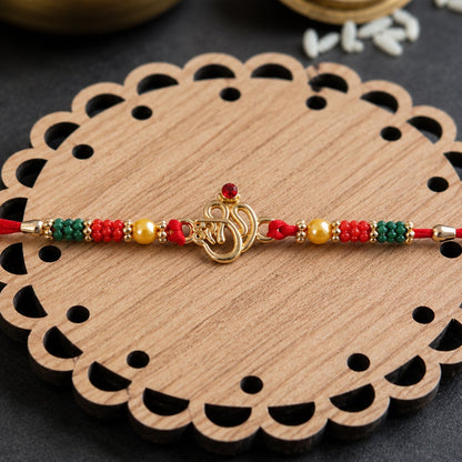 Golden Om (?) Rakhi with Red & Green Crystal Beads