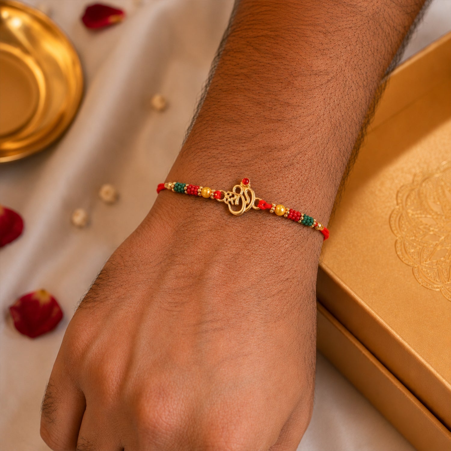 Golden Om (?) Rakhi with Red & Green Crystal Beads