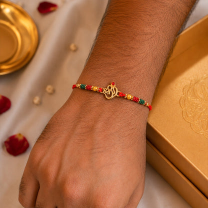 Golden Om (?) Rakhi with Red & Green Crystal Beads