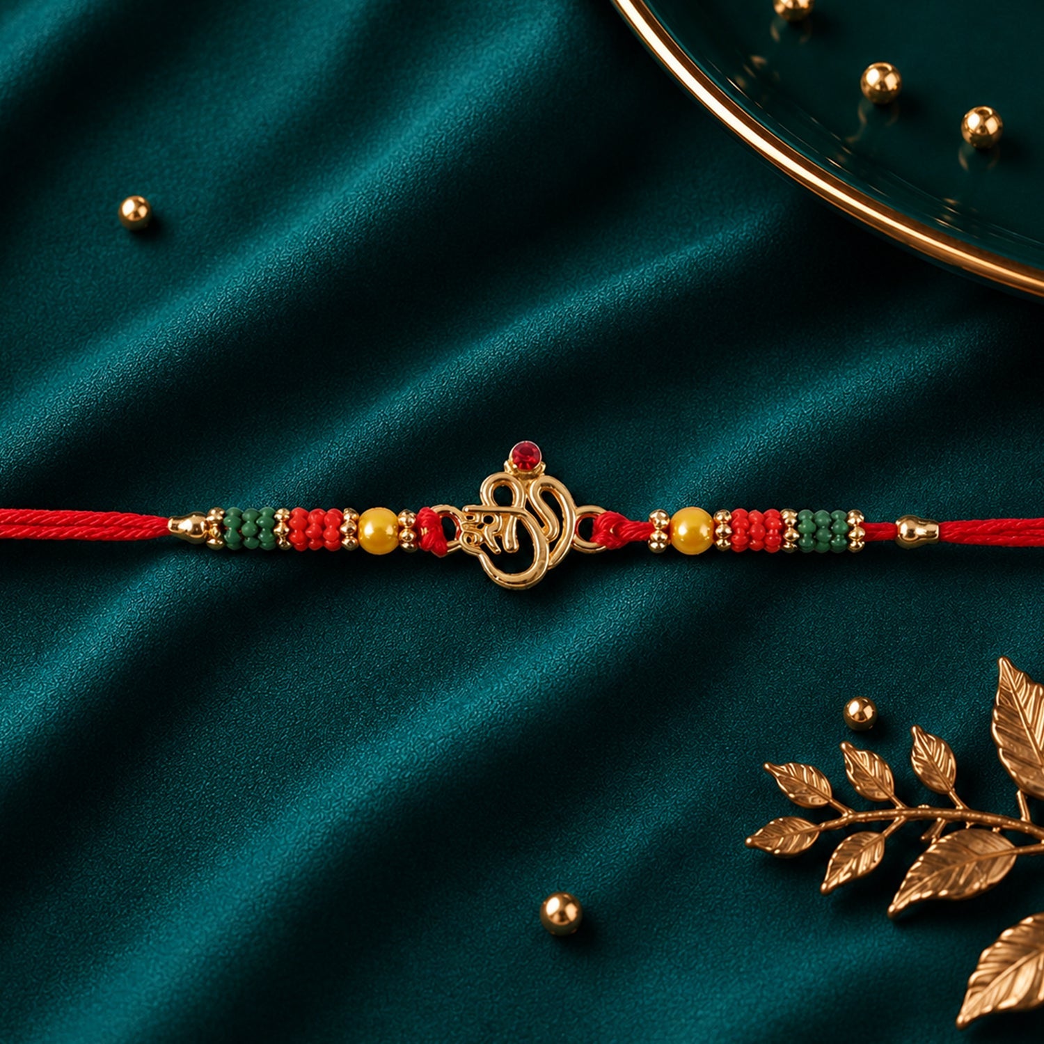 Golden Om (?) Rakhi with Red & Green Crystal Beads