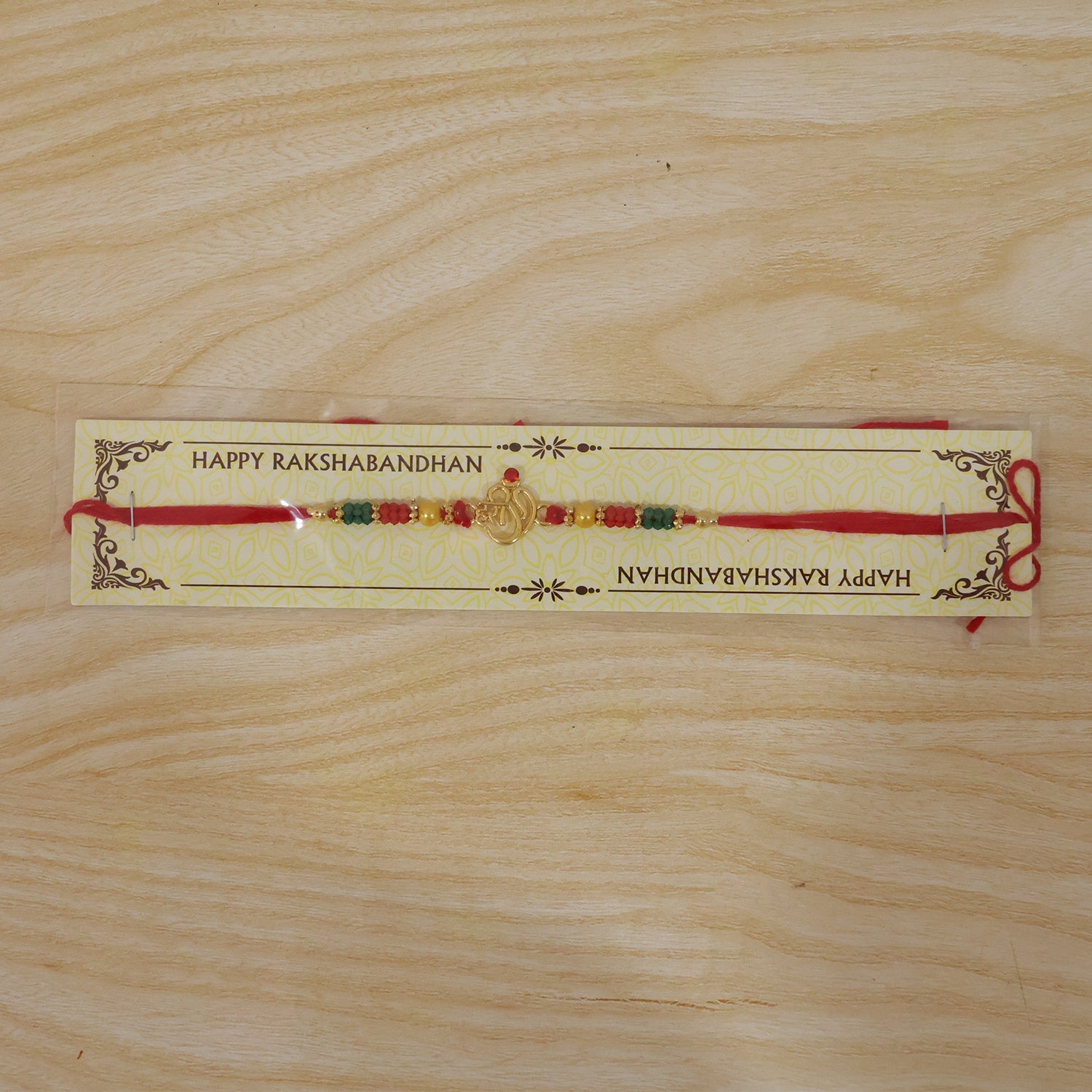 Golden Om (?) Rakhi with Red & Green Crystal Beads