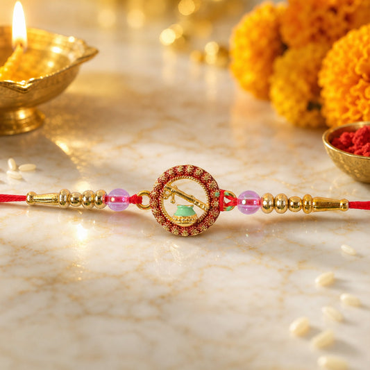 A red thread with a gold and red circular charm featuring a Krishna flute and pot, flanked by gold and pink beads, on a