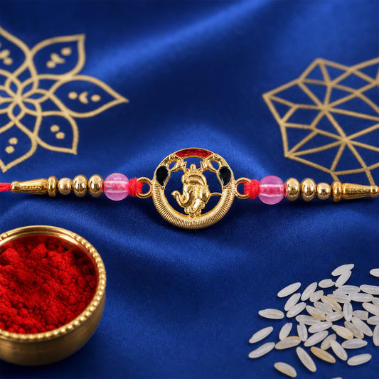 A gold-toned Ganesha motif with red and black accents is centered on a red thread, flanked by gold and pink beads, set on a