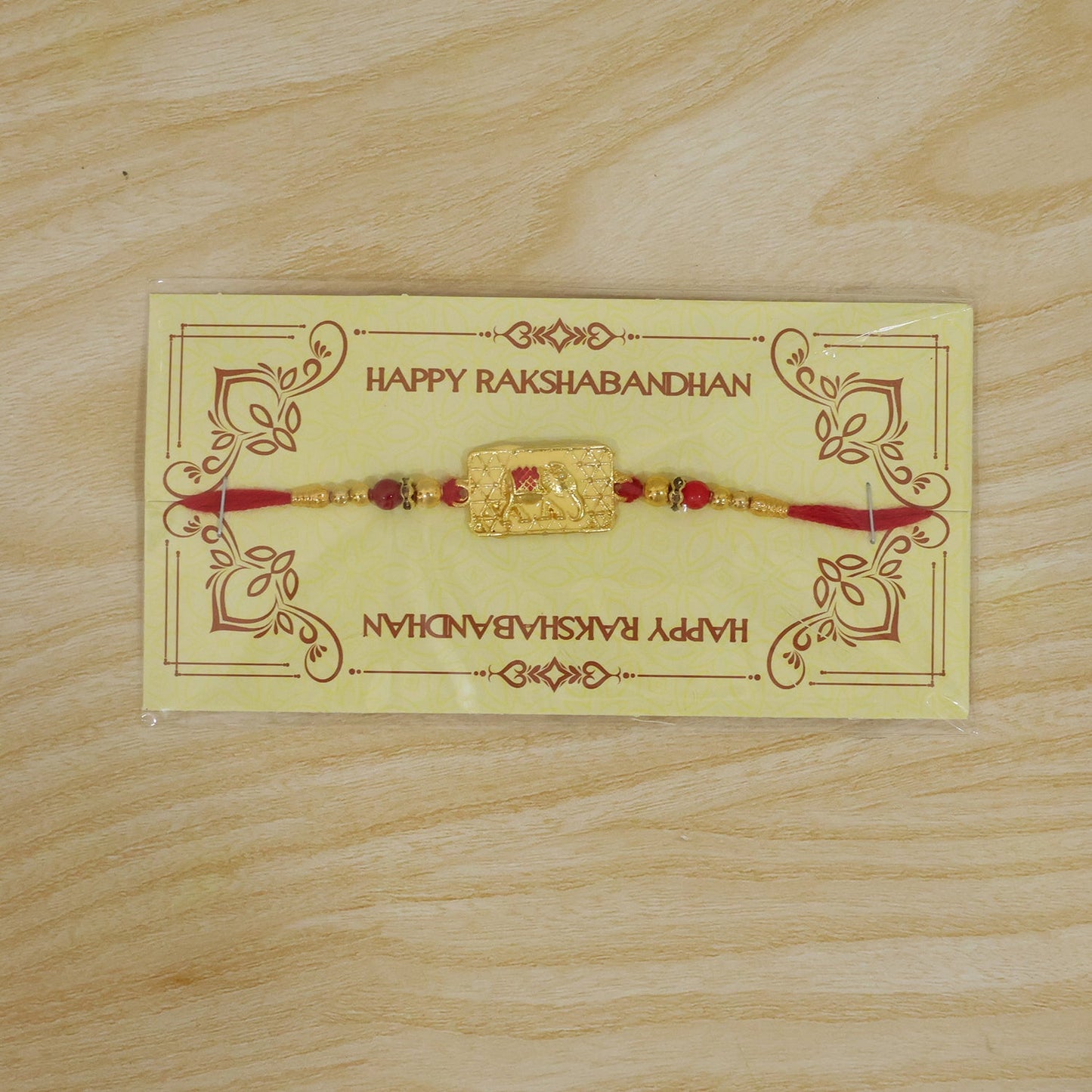 The gold elephant charm with red and gold beads on a red thread is displayed on a yellow card with
