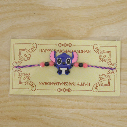 A blue cartoon character charm with pink and black beads on a purple and pink thread, displayed on a yellow card with