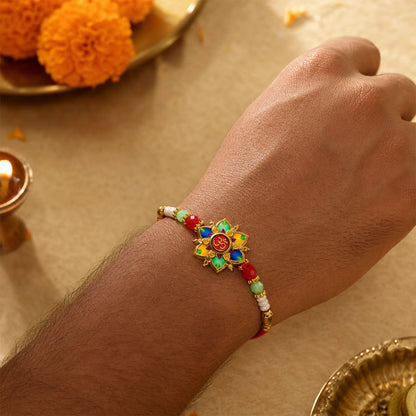 The multicolor lotus and Om design, with red, green, and white beads on a red thread, is worn on a person's wrist, with a