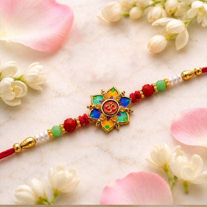 The colorful lotus and Om design, with red, green, and white beads on a red thread, is displayed on a white marble surface